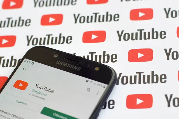 Aplicación de Youtube en pantalla Samsung smartphone en banner de papel con pequeños logotipos e inscripciones de youtube. YouTube es la subsidiaria de Google y la plataforma de intercambio de videos más popular de Estados Unidos — Foto de Stock