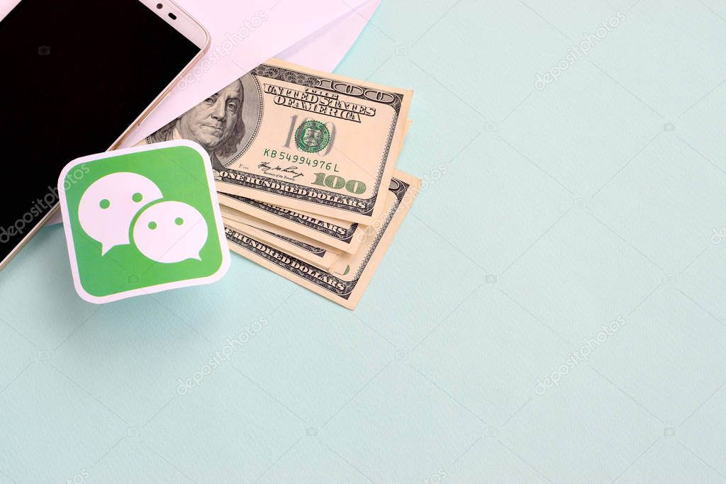 NY, USA - DECEMBER 26, 2019: Wechat paper logo lies with envelope full of dollar bills and smartphone