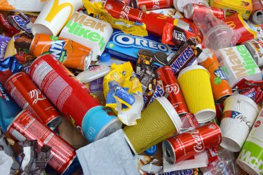 Ünlü yiyecek ve içecek üreticilerinin yenilebilir ürünlerinden bir sürü tek kullanımlık çöp yığını. Soda kutuları ve çikolata ambalajları yığınla.