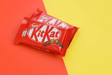 Kırmızı ambalajlı Kit Kat çikolataları sarı ve kırmızı arka planda yatar. Kit Kat, Birleşik Krallık 'ta Rowntree' s of York tarafından yaratıldı ve şimdi küresel olarak Nestle tarafından üretiliyor.