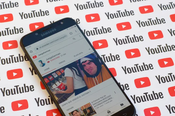 JuegaGerman official youtube channel on smartphone screen on paper youtube background. — Stock Photo, Image