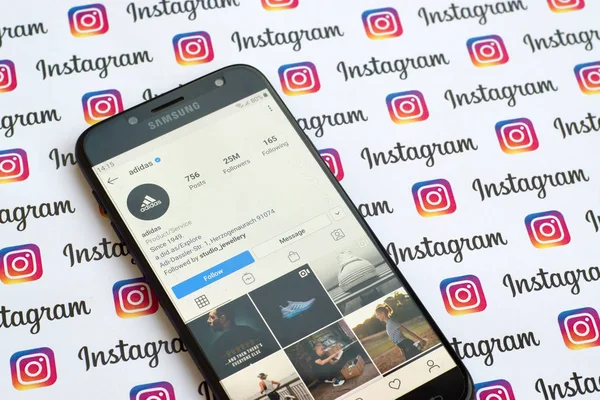 Oficjalne konto na Instagramie Adidas na ekranie smartfona na papierowym banerze Instagram. — Zdjęcie stockowe