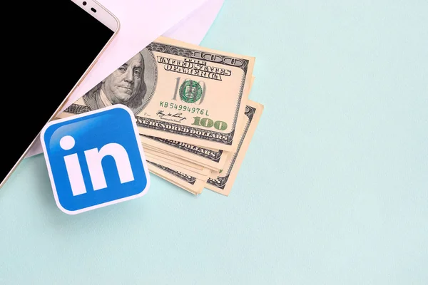 Linkedin λογότυπο χαρτί βρίσκεται με το φάκελο γεμάτο δολάρια λογαριασμούς και smartphone — Φωτογραφία Αρχείου