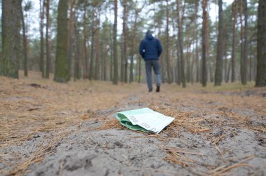 Young man loses his euro money bills on Russian autumn fir wood path. Carelessness and losing money concept clipart