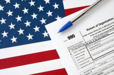 Form 990 Return of organization exempt from income tax and blue pen on United States flag. Internal revenue service tax form clipart