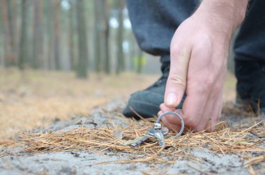 Male hand picking up lost keys from a ground in autumn fir wood path. The concept of finding a valuable thing and good luck clipart