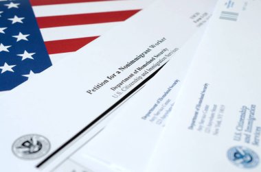 I-129 Petition for a nonimmigrant worker blank form lies on United States flag with envelope from Department of Homeland Security clipart