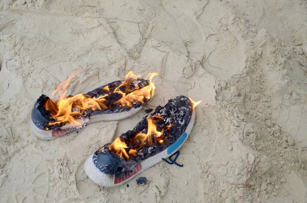 Zapatillas deportivas quemadas o zapatos de gimnasio en el puesto de fuego en la costa de la playa de arena. Atleta agotado. Ejercicio físico durante el concepto de entrenamiento — Foto de Stock