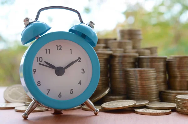 Blue alarm clock on big amount of shiny ukrainian old 1 hryvnia coin stacks close up on blurred green trees backdrop. The concept of financial planning and business time management — 스톡 사진