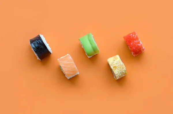 Verschiedene asiatische Sushi-Rollen auf orangefarbenem Hintergrund. Minimalismus von oben flach lag mit japanischem Essen — Stockfoto