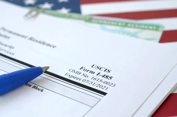 I-485 Application to register permanent residence or adjust status form and green card from dv-lottery lies on United States flag with blue pen from Department of Homeland Security