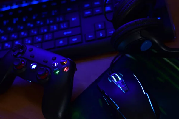 Современная геймпад и игровая мышь лежат с клавиатурой и наушниками на столе в темной сцене игровой комнаты. Концепция сообщества игроков онлайн-игр — стоковое фото