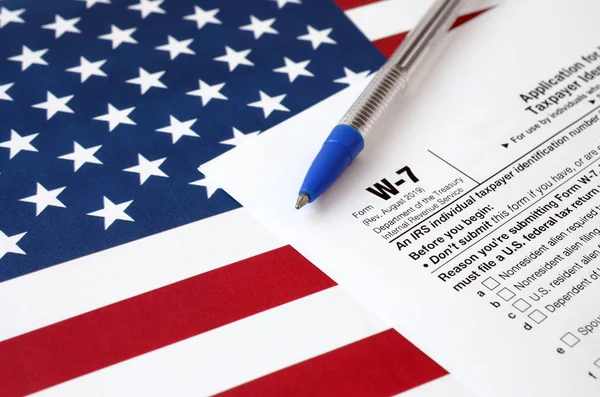 Έντυπο W-7 Αίτηση για τη χορήγηση ΑΜ Ατομικού αριθμού φορολογικού μητρώου και μπλε στυλό με σημαία Ηνωμένων Πολιτειών. Έντυπο φορολογίας των εσωτερικών εσόδων — Φωτογραφία Αρχείου