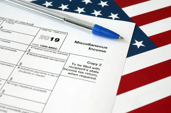 Форма 1099-misc Різний дохід і синя ручка на прапорі США. Податкова форма внутрішнього доходу. — стокове фото