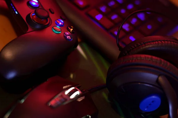 Modern gamepad and gaming mouse lies with keyboard and headphones on table in dark playroom scene. Background composition for video gaming and esports design