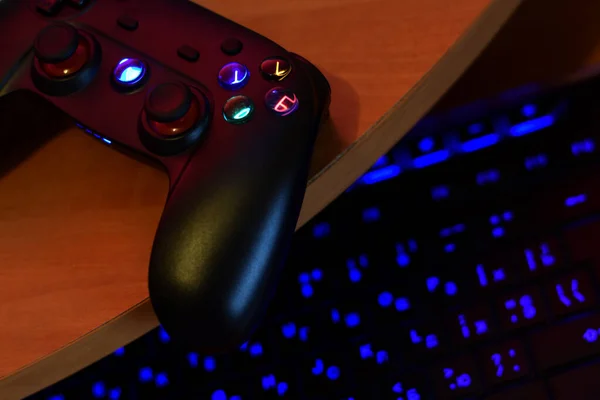 Modernes Gamepad liegt mit PC-Tastatur auf dem Tisch in dunkler Spielzimmerszene in Großaufnahme. Lässt Videospiele mit Freunden spielen — Stockbild Modernes Gamepad liegt mit PC-Tastatur auf dem Tisch in dunkler Spielzimmerszene. Lässt Videospiele mit Freunden spielen — Stockfoto