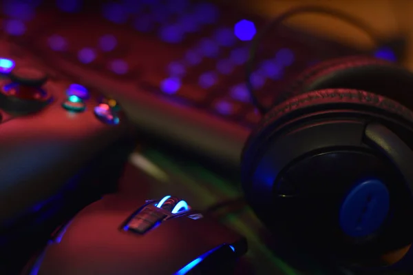 Μοντέρνο gamepad και gaming mouse βρίσκεται με πληκτρολόγιο και ακουστικά στο τραπέζι στο σκοτεινό playroom σκηνή. Βιντεοπαιχνίδια προκλήσεις και διαγωνισμούς έννοια — Φωτογραφία Αρχείου