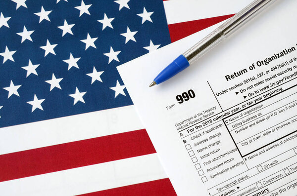 Form 990 Return of organization exempt from income tax and blue pen on United States flag. Internal revenue service tax form