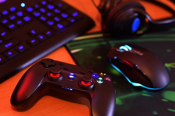 O gamepad moderno e o mouse de jogo estão com teclado e fones de ouvido na mesa na cena escura da sala de jogos. Conceito de desafios e competições de jogos de vídeo — Fotografia de Stock