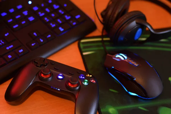 Nowoczesny gamepad i mysz do gier leży z klawiatury i słuchawek na stole w ciemnej scenie pokoju zabaw. Zagrajmy w gry wideo wraz z koncepcją znajomych — Zdjęcie stockowe