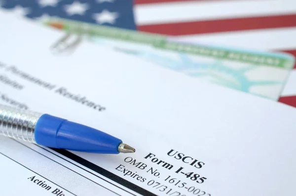 I-485 Application to register permanent residence or adjust status form and green card from dv-lottery lies on United States flag with blue pen from Department of Homeland Security