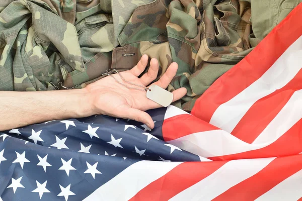 Silvery military beads with dog tag and hand of dead soldier on United States fabric flag and camouflage uniform — Stock Photo, Image