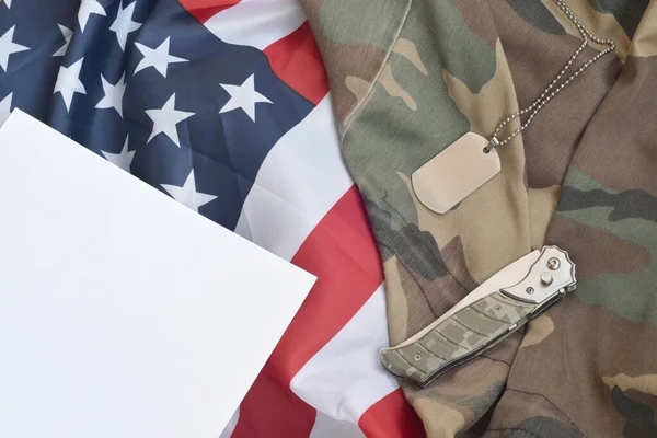 Army dog tag token and knife lies on Old Camouflage uniform and folded United States Flag — Stock Photo, Image