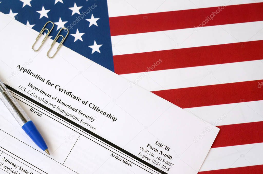 N-600 Application for Certificate of Citizenship blank form lies on United States flag with blue pen from Department of Homeland Security