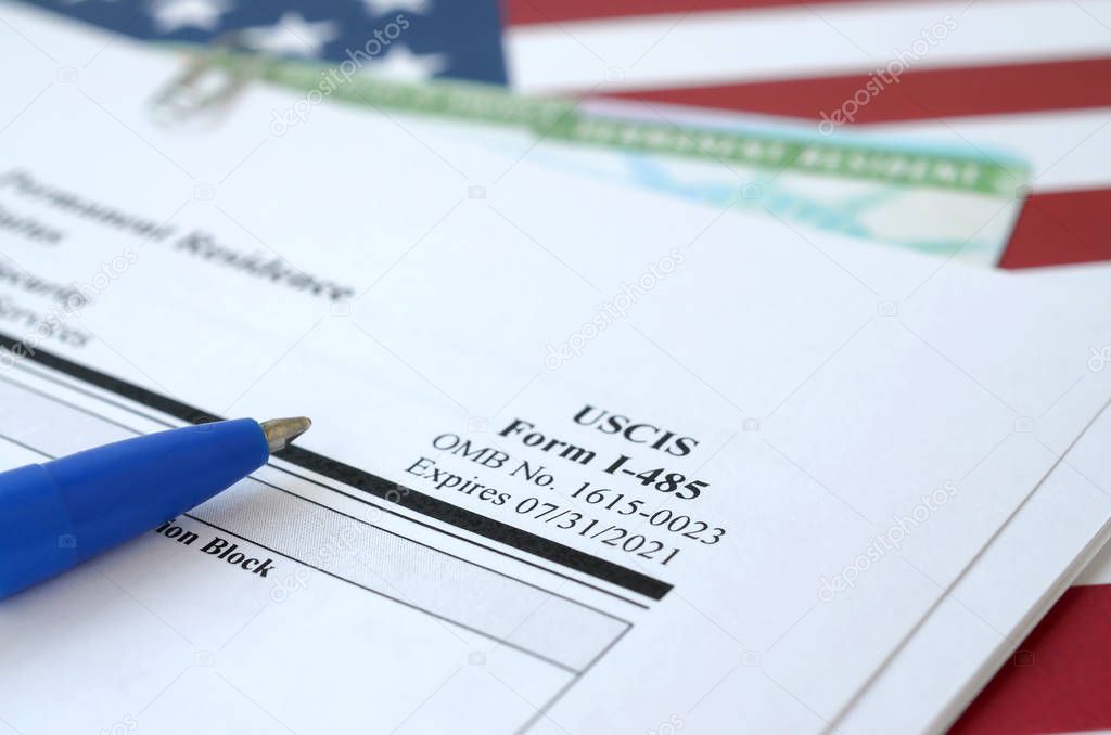 I-485 Application to register permanent residence or adjust status form and green card from dv-lottery lies on United States flag with blue pen from Department of Homeland Security