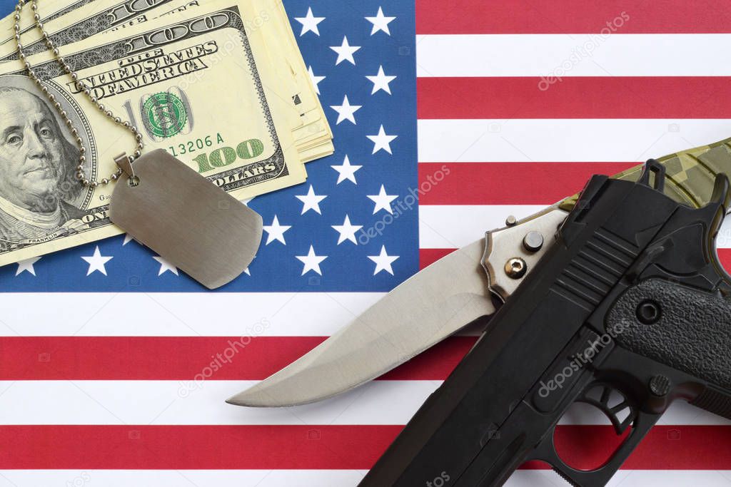 Close up dollar money with weapons and military badges on United States flag. Military forces, financing and national service concept