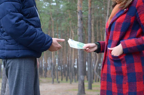 Girl transfers euro bills to the hands of a young guy in forest. Concept of robbery or illegal deal transaction — 스톡 사진
