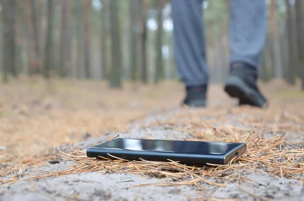Młody człowiek gubi smartfona na rosyjskiej jesiennej ścieżce z drewna jodłowego. Niedbałość i utrata drogiej koncepcji urządzenia mobilnego — Zdjęcie stockowe