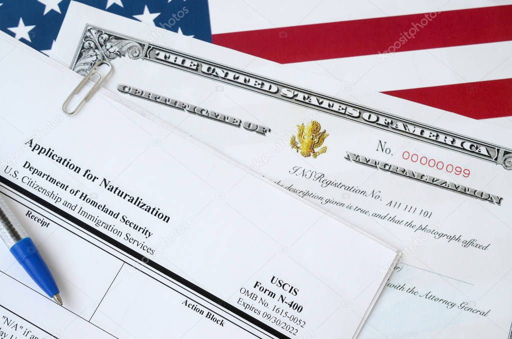 N-400 Application for Naturalization and Certificate of naturalization lies on United States flag with blue pen from Department of Homeland Security