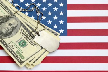 Ordu kimlik madalyonları ve Amerikan bayrağında dolar banknotları. Askeri emeklilik, orduda maaş veya askeri sigorta.