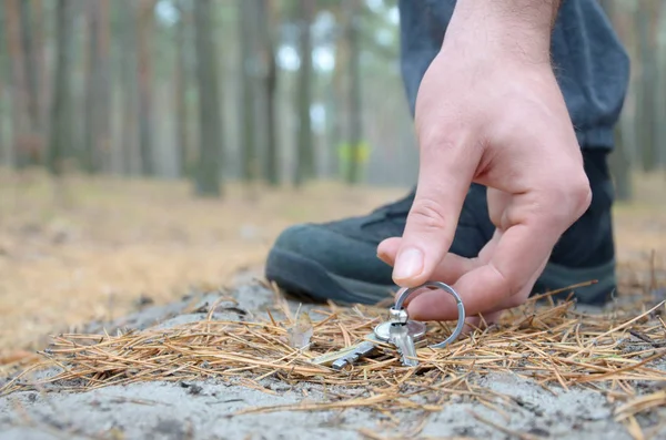 Mão masculina pegando chaves perdidas de um chão no caminho de madeira de abeto de outono. O conceito de encontrar uma coisa valiosa e boa sorte — Fotografia de Stock