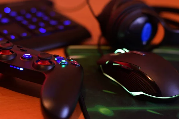 La manette moderne et la souris de jeu se trouvent avec le clavier et le casque sur la table dans la scène sombre de salle de jeux. Concept de jeu d'équipe coopératif — Photo