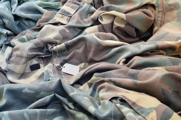 Etiqueta de perro ejército perdido y vacío se encuentra en la pila de ropa de camuflaje doblado — Foto de Stock