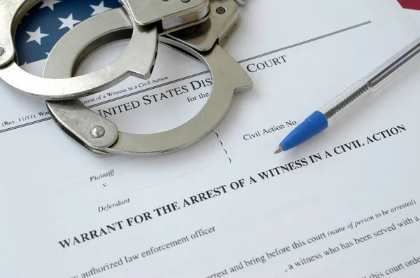 Окружной суд выписал ордер на арест свидетеля в гражданском иске с наручниками и синей ручкой на флаге США. Разрешение на арест свидетеля — стоковое фото