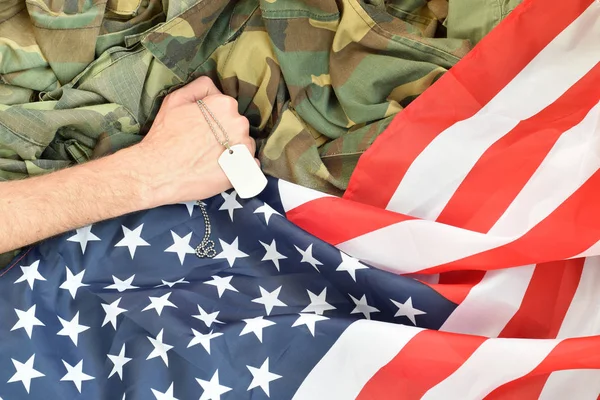 Masculino mão detém cão tag no EUA bandeira e militar uniforme fundo — Fotografia de Stock