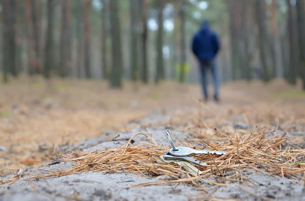 Young man loses his keys bunch on Russian autumn fir wood path. Carelessness and losing keys concept — Stock Photo, Image