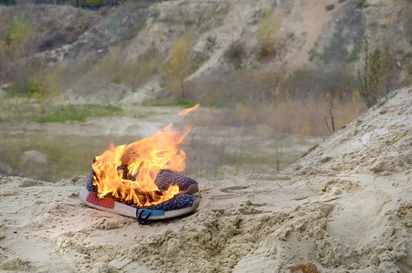 Zapatillas deportivas quemadas o zapatos de gimnasio en el puesto de fuego en la costa de la playa de arena. Atleta agotado. Ejercicio físico durante el concepto de entrenamiento — Foto de Stock