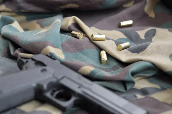 9 мм пули и пистолет лежат на сложенной камуфляжной зеленой ткани. Набор предметов для стрельбы или набор для самообороны — стоковое фото