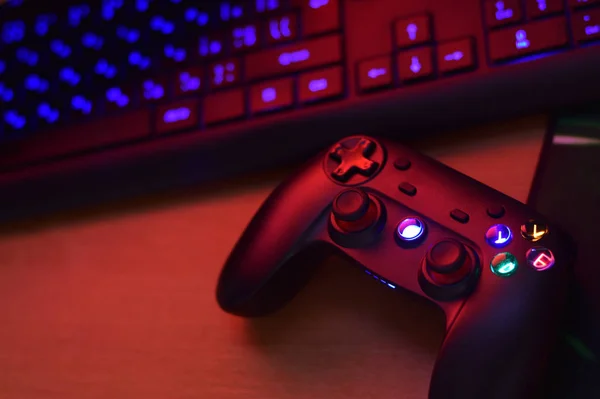 O gamepad moderno está com o teclado do PC na mesa na cena escura da sala de jogos. Gameplay streaming e conceito de vídeo game walkthroughts — Fotografia de Stock