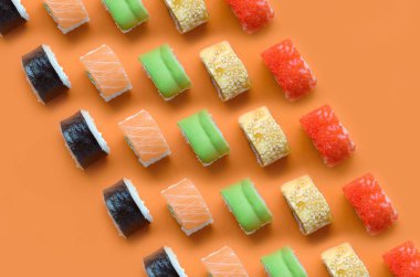 Turuncu arka planda farklı Asya suşi çeşitleri var. Minimalizm üst görünüm düz Japon yemekleri ile yatıyordu