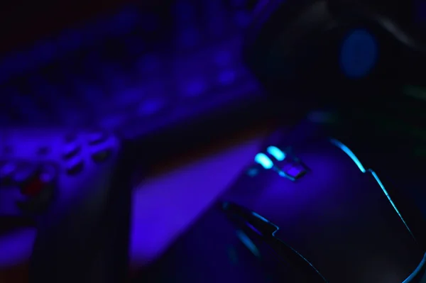 Сучасна ігрова та ігрова миша лежить з клавіатурою та навушниками на столі у темній ігровій кімнаті. Дає змогу грати у відеоігри разом з концепцією друзів — стокове фото