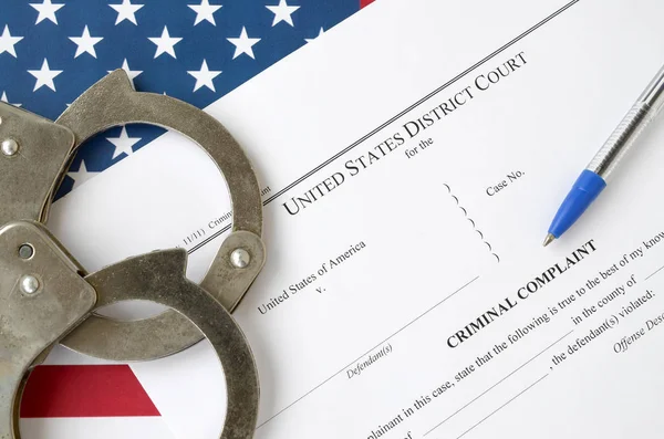 District Court Criminal complaint court papers with handcuffs and blue pen on United States flag