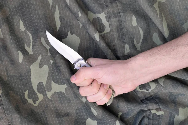 Ręka z małym nożem na tle tkaniny kamuflażu. Koncepcja użycia noża w taktyce walki między żołnierzami — Zdjęcie stockowe
