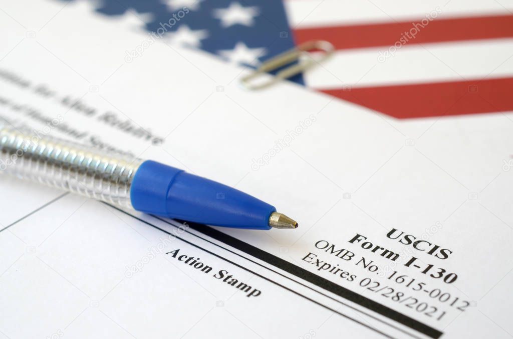 I-130 Petition for alien relative blank form lies on United States flag with blue pen from Department of Homeland Security