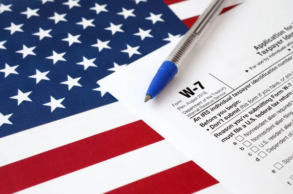 Form W-7 Application for IRS Individual taxpayer identification number and blue pen on United States flag. Internal revenue service tax form — 스톡 사진