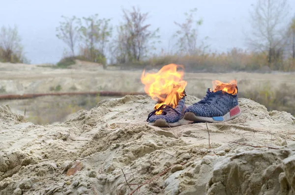 Zapatillas deportivas quemadas o zapatos de gimnasio en el puesto de fuego en la costa de la playa de arena. Atleta agotado. Ejercicio físico durante el concepto de entrenamiento — Foto de Stock